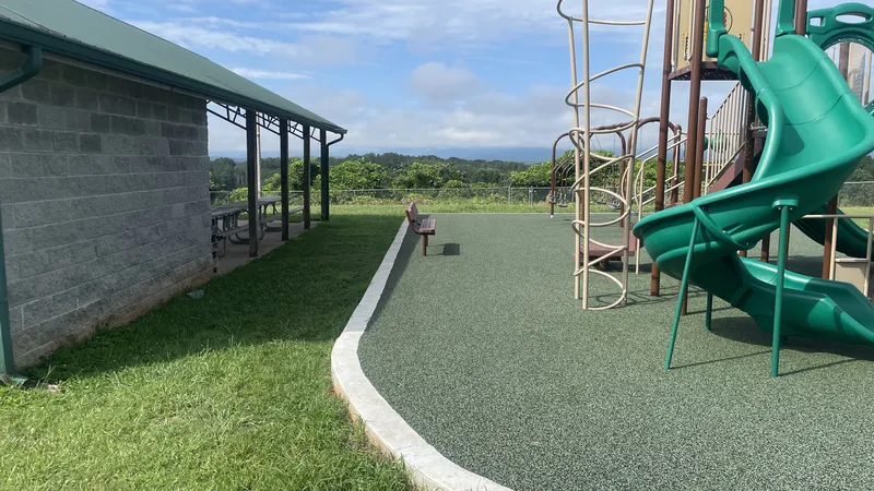 Poured rubber safety surfacing bordering a playground, with a bench and a covered pavilion nearby.