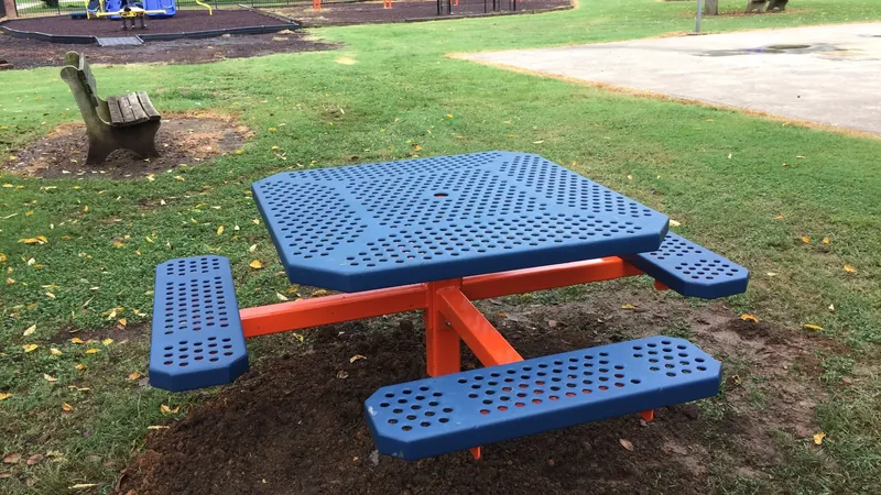 A blue-and-orange accessible picnic table set on a lawn near a playground.
